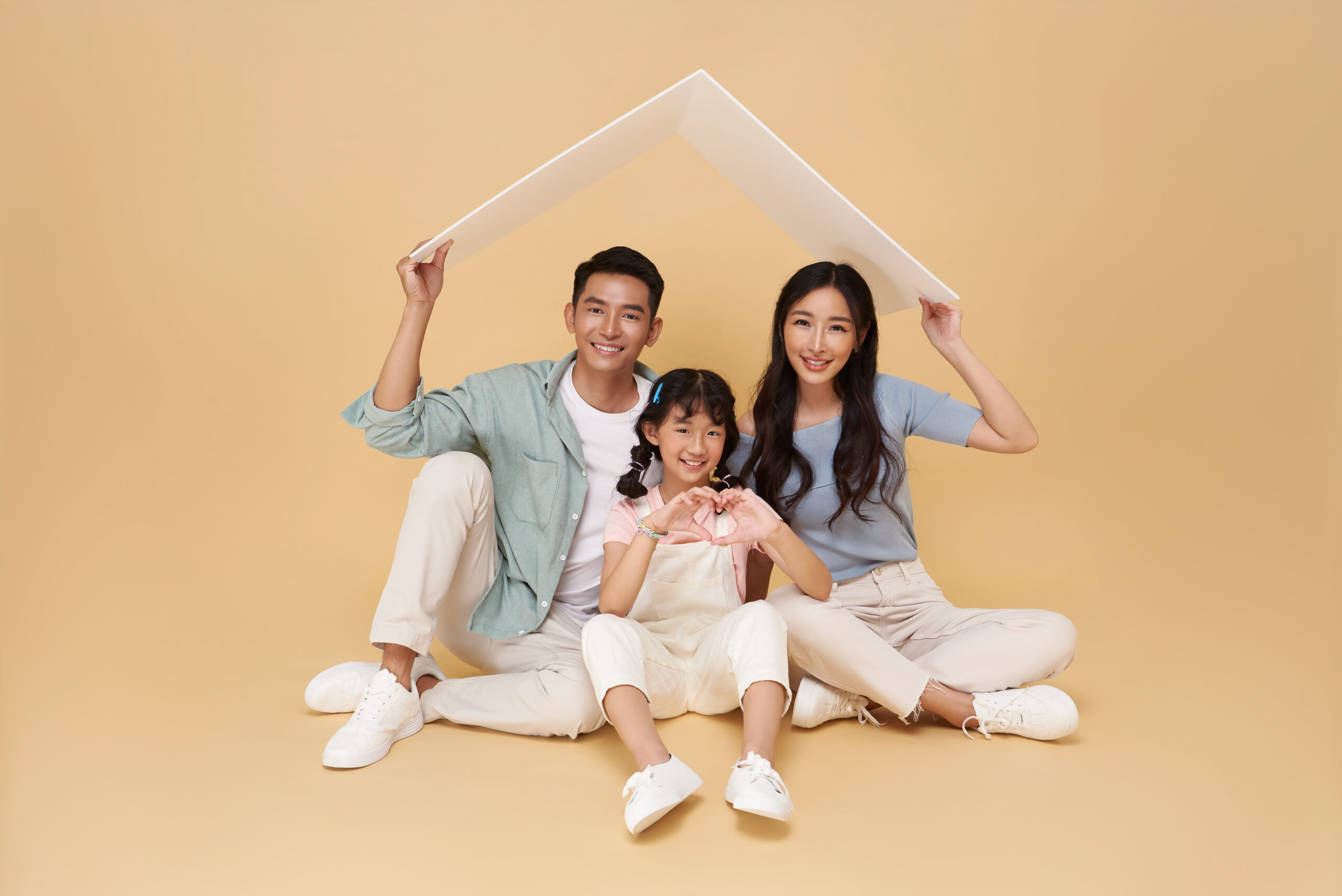 Happy asian family forming house roof with their hands at home isolated on nude color background. Insurance concept